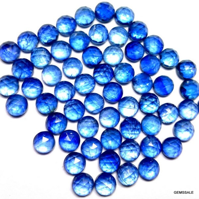 May include: A collection of round, faceted blue gemstones. The stones have a light blue color with a white, iridescent sheen. The stones are approximately 1 cm in diameter.