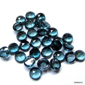 May include: A collection of 25 faceted, round, blue topaz gemstones. The stones are approximately 10mm in diameter and have a variety of shades of blue.