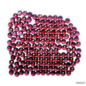 Peut inclure: Une collection d'environ 100 pierres précieuses rondes, facettées et rouges. Les pierres précieuses sont disposées en forme de demi-cercle, avec les plus grosses pierres au centre et les plus petites pierres sur les bords.