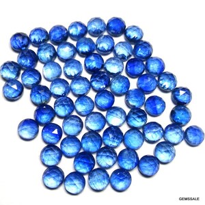 May include: A large pile of round, faceted blue gemstones. The gemstones are all approximately the same size and shape, and they have a shiny, polished finish.