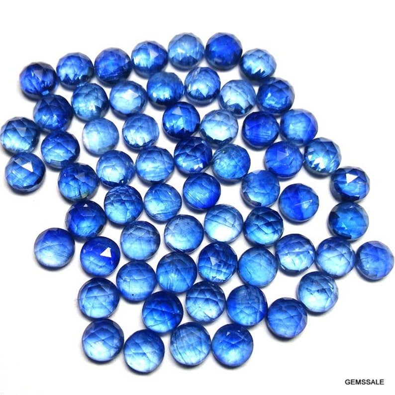 May include: A large pile of round, faceted blue gemstones. The gemstones are all approximately the same size and shape, and they have a shiny, polished finish.