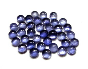 May include: A collection of round, blue-purple gemstones, also known as iolite, arranged in a pile. The stones have a smooth, polished finish and a slightly iridescent sheen.