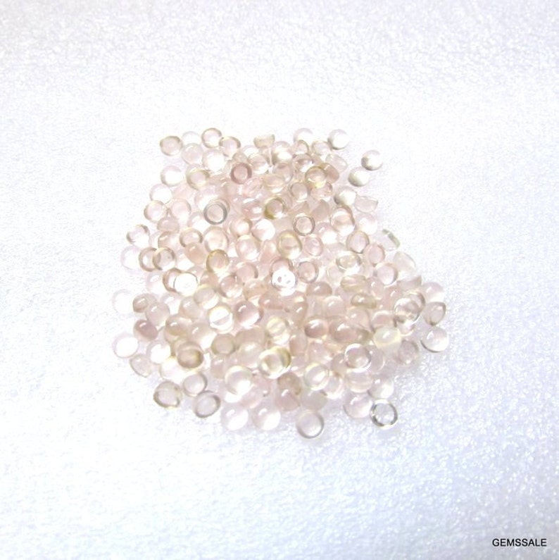 May include: A pile of small, round, translucent pink gemstones. The gemstones are smooth and have a slight shimmer.