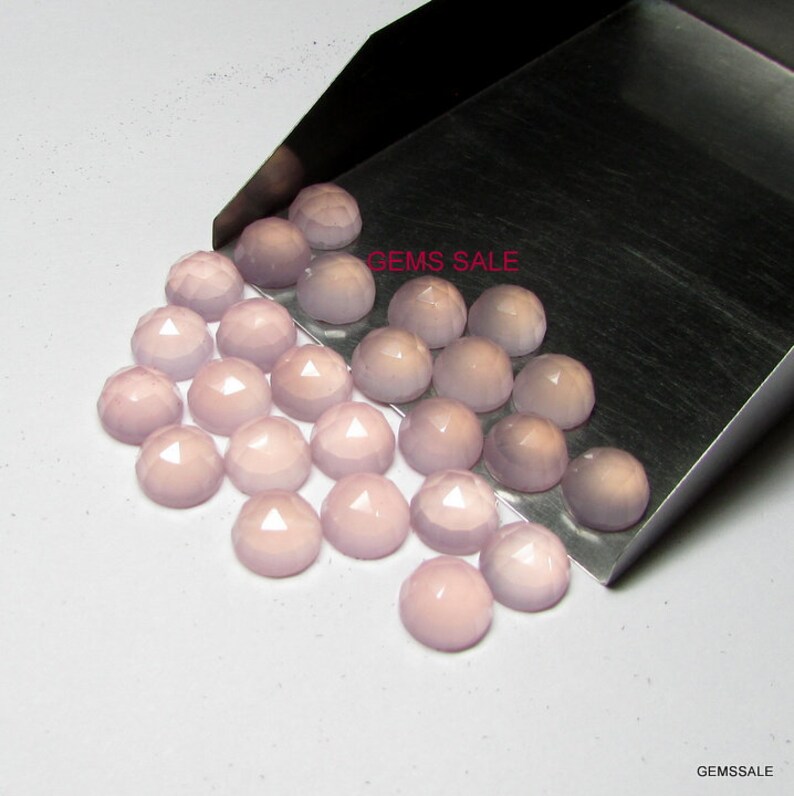 Puede incluir: Un grupo de 25 cabujones redondos de piedra preciosa de color rosa p&aacute;lido y facetados. Los cabujones est&aacute;n dispuestos en semic&iacute;rculo sobre una superficie de metal plateado. El texto "GEMS SALE" es visible en la esquina superior derecha de la imagen.
