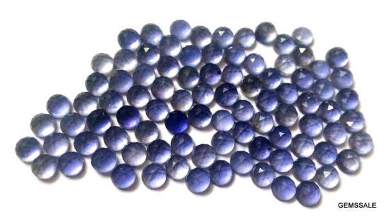 May include: A collection of round, faceted, purple gemstones. The stones are arranged in a loose pile, with some overlapping. The stones are all approximately the same size and shape.