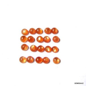 May include: A collection of 18 round, orange sunstone cabochons. The stones are arranged in rows and are all approximately the same size.