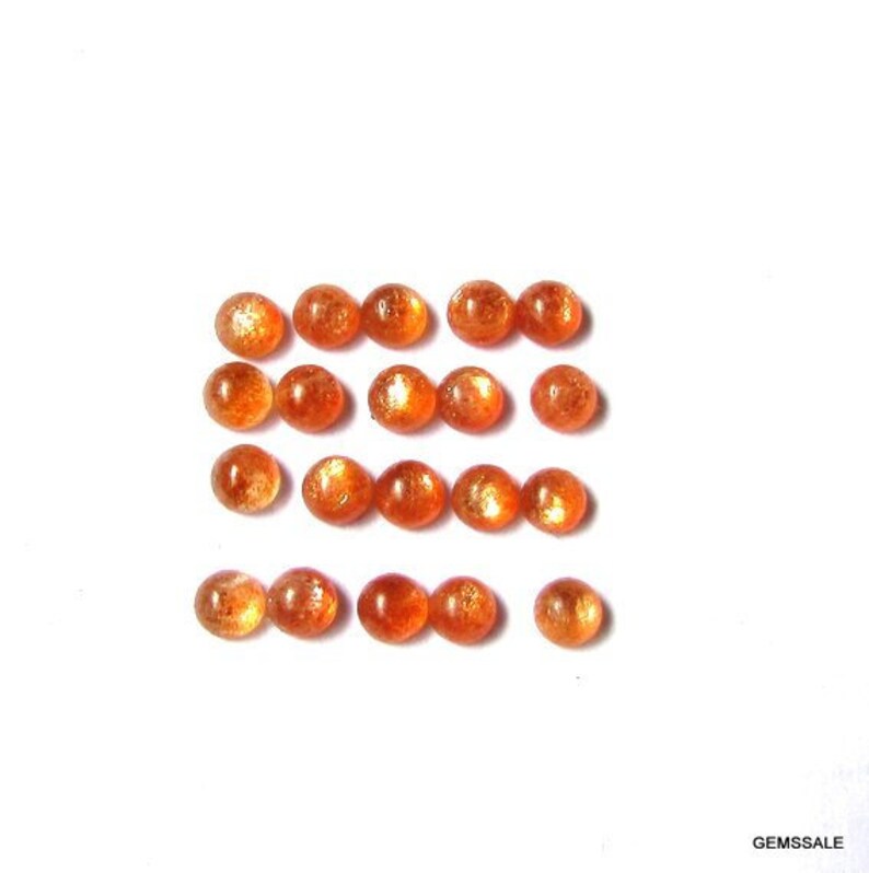 May include: A collection of 18 round, orange sunstone cabochons. The stones are arranged in rows and are all approximately the same size.