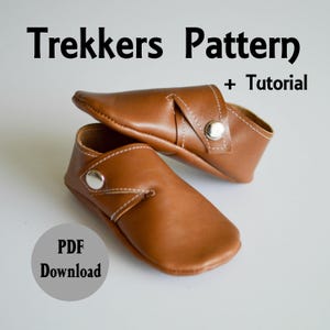 May include: A pair of brown leather baby shoes with a strap and button closure. The shoes are on a white background. The text "Trekkers Pattern + Tutorial" and "PDF Download" is visible in the image.