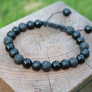May include: Black beaded bracelet with alternating black onyx and lava rock beads. The bracelet has a black cord with a sliding knot for adjusting the size.