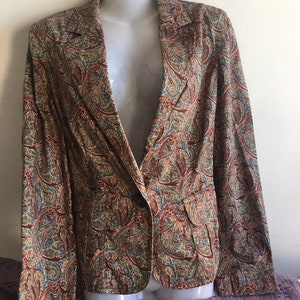 May include: A paisley-patterned blazer in shades of brown, red, blue, and green. The jacket has a notched collar, two front pockets, and a single-button closure. The blazer is displayed on a white mannequin.