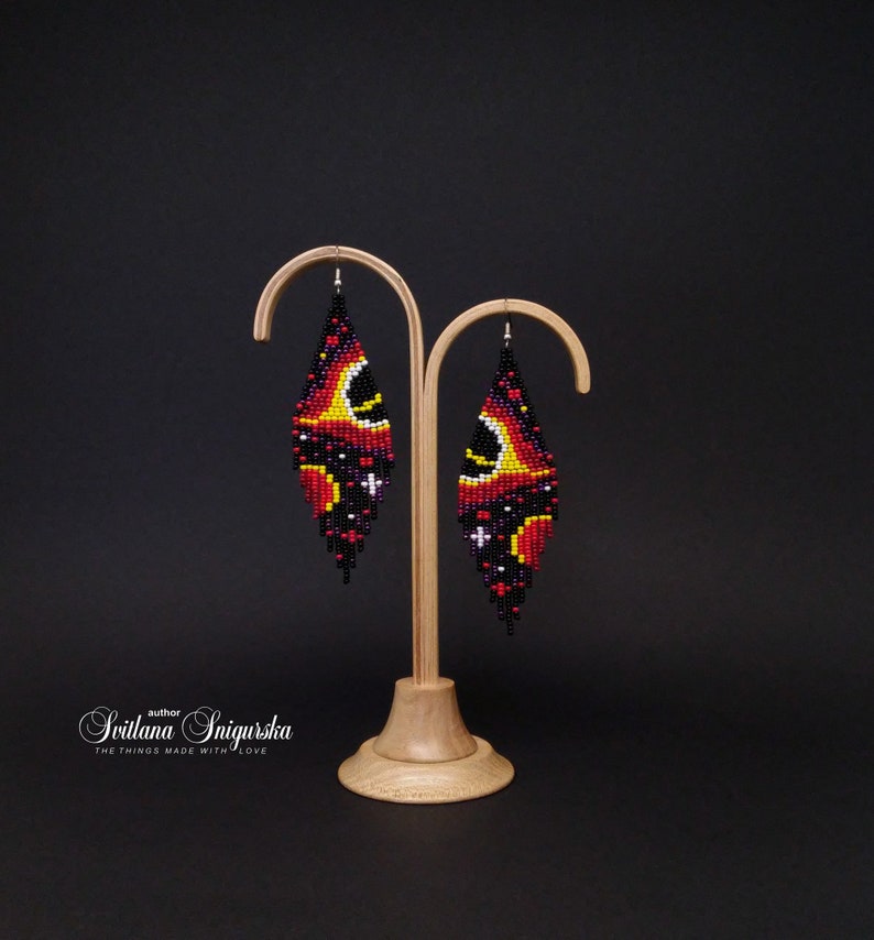 Handwoven black hole beaded earrings with red, gold and black cosmic galaxy design, long fringe seed bead statement jewelry on silver-plated hooks.