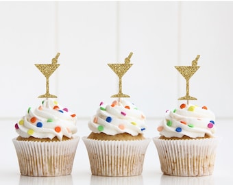 May include: Three cupcakes with white frosting and colorful sprinkles topped with gold glitter martini glass cupcake toppers.
