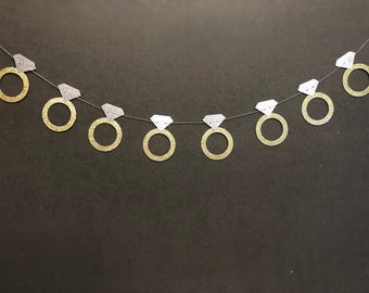May include: A gold and silver glitter ring garland with a string of connected rings. The rings are in the shape of engagement rings with diamonds.