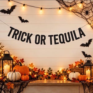 May include: A black glittery banner with the text TRICK OR TEQUILA suspended against a white wall. The scene includes orange and white pumpkins, two black lanterns with lit candles, autumn leaves, string lights, and black paper bats.