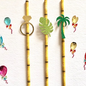 May include: Three yellow striped paper straws with decorative toppers. The straws have a gold glitter ring, a green glitter palm leaf, and a green glitter palm tree. There are also several blue, red, and gold glitter balloons scattered around the straws.