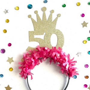 May include: Gold glitter crown with the number 50 on top of a pink headband with pink tissue paper fringe.