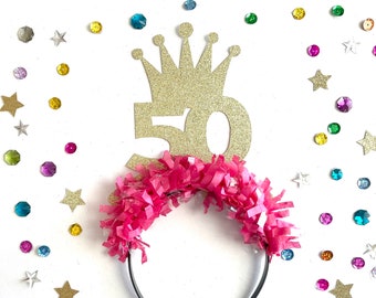 May include: Gold glitter crown with the number 50 on top of a pink headband with pink tissue paper fringe.
