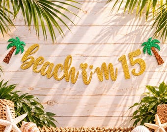 May include: A gold glitter banner with the text beach i'm 15, flanked by two green and brown glitter palm tree cutouts. The banner is displayed against a light wood background with green palm leaves and white seashells at the bottom.