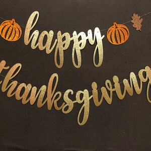 Puede incluir: Una pancarta dorada con purpurina con las palabras "happy thanksgiving" y dos calabazas naranjas con purpurina con hojas marrones con purpurina.