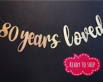 May include: Gold glitter banner with the text "80 years loved".
