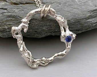 Molten silver circle necklace set with a cornflower blue Sapphire gemstone, organic silver pendant