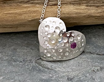 Silver heart pendant set with a bright pink Sapphire and hammered and drilled to add sparkle