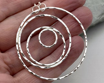 Puede incluir: Un conjunto de cuatro pendientes de aro martillados de plata de diferentes tamaños. Los pendientes están hechos de plata de ley y tienen un acabado martillado. Los pendientes son perfectos para añadir un toque de estilo a cualquier atuendo.