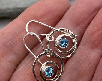 Hammered silver round dangle earrings set with a sparkly blue Topaz gemstone.