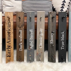 K&ouml;nnte beinhalten: Zehn Holz-Kleiderst&auml;nder mit verschiedenen Beizfarben und -oberfl&auml;chen. Die Farben sind unbehandelt, halbtransparent wei&szlig; gebeizt, Early American, dunkel Nussbaum, gealtertes Fass, klassisches Grau, Ebenholz, echtes Schwarz, abgenutztes Marineblau und Marineblau.