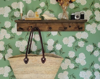 May include: A wooden shelf with a brown leather tote bag hanging from a hook. The shelf is decorated with a candle, a crystal, a small wooden figure, and a bone. The wall behind the shelf is covered in green wallpaper with a white floral pattern.