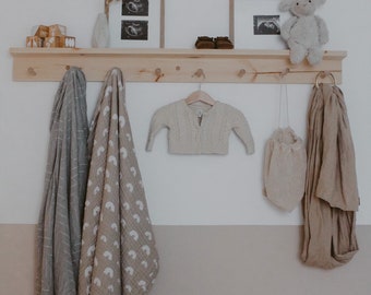 May include: A wooden shelf with hooks hangs on a wall. Two framed ultrasound images are on the shelf. A stuffed animal, a knitted sweater, a woven bag, and two blankets hang from the hooks.