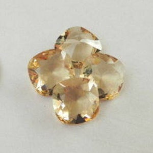 May include: A silver coin and four light orange-colored gemstones arranged in a clover shape. The coin has a profile of a person and the words "IN GOD WE TRUST" and the year 1936. The gemstones are oval-shaped and faceted.