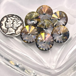 May include: A collection of seven faceted, round crystals with a shimmering, iridescent finish. A silver coin with the year 1936 is next to the crystals. The crystals are in a clear, glass dish.