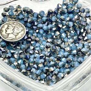 May include: A collection of faceted blue beads in a clear glass dish, with a silver coin from 1936. The beads have a metallic sheen and are strung on a wire. The beads are a mix of light and dark blue.