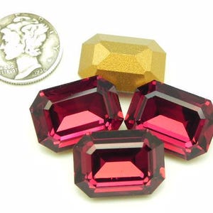 May include: An assortment of gemstones and a silver coin. Four faceted, rectangular, deep red gemstones are arranged with one gold-colored gemstone. The coin is silver and dated 1936.