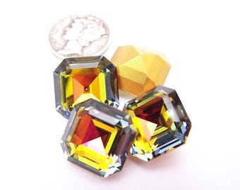 Puede incluir: Primer plano de tres gemas facetadas de corte cuadrado con una mezcla de tonos amarillos, naranjas y rojos. También se ve una forma geométrica dorada y una moneda de plata. Las gemas tienen una cualidad iridiscente.