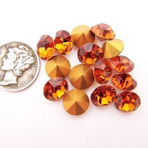 Puede incluir: Un conjunto de pedrería facetada de color naranja y dorado, con una moneda de plata de 1936 para comparar el tamaño. Las piedras preciosas tienen un corte brillante y multifacético, que refleja la luz. La moneda tiene un diámetro de aproximadamente 1,9 cm.
