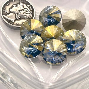 Puede incluir: Primer plano de varios cristales redondos facetados y una moneda de plata. Los cristales tienen una mezcla de facetas amarillas, azules y transparentes. Un cristal es de color gris claro sólido. La moneda es una moneda de diez centavos Mercury de plata de 1936.