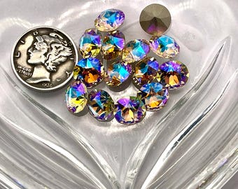 May include: A collection of iridescent oval-shaped crystals and a single round crystal are displayed in a clear, heart-shaped glass dish. A silver 1936 Mercury dime is also present. The crystals reflect a spectrum of colors, including yellow, blue, and purple.