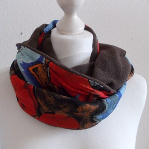 Peut inclure: Un tour de cou en polaire marron avec une doublure en tissu à motifs colorés. Le motif présente des formes abstraites rouges, bleues et orange.