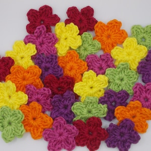 Può includere: Una collezione di fiori colorati all'uncinetto in varie tonalità di rosso, giallo, arancione, verde, viola e rosa. Questi abbellimenti floreali fatti a mano sono ideali per progetti di artigianato.