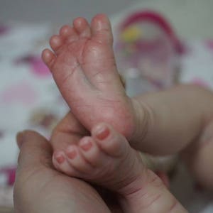May include: Close-up of a baby's feet, showing the detail of the realistic silicone skin. The feet are soft and plump, with tiny toes and delicate wrinkles.