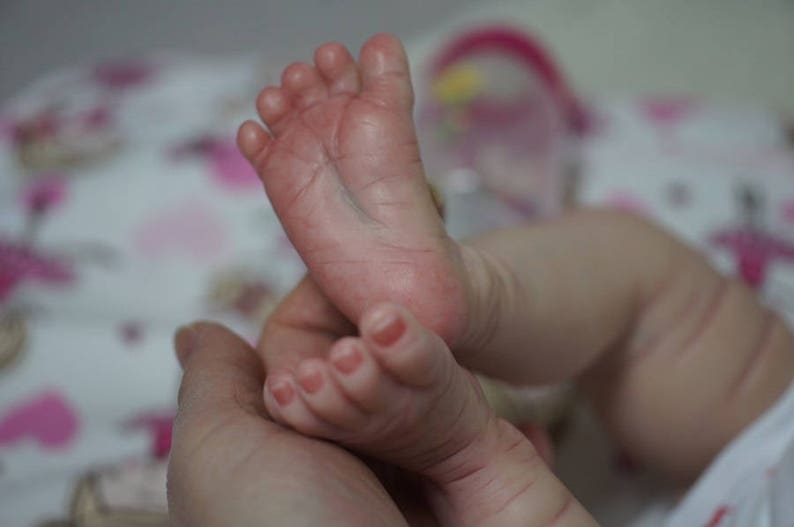May include: Close-up of a baby's feet, showing the detail of the realistic silicone skin. The feet are soft and plump, with tiny toes and delicate wrinkles.