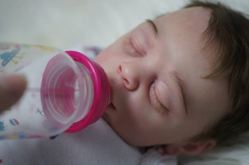May include: A baby is sleeping while being fed from a clear plastic bottle with a pink and white nipple.
