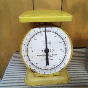 May include: A yellow vintage kitchen scale with a white face and black markings. The scale reads "Weighs 25 Pounds by Ounces 11 kilograms 50 grams 190  del NOT LEGAL FOR TRADE".