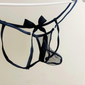 May include: Navy blue lingerie set featuring a sheer mesh panel and a decorative bow. The delicate design includes thin straps and a ring detail. The lingerie is suspended against a plain white background.