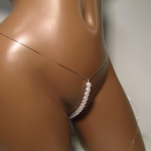 May include: A delicate, silver-toned body chain with a string of white pearls. The pearls cascade down the front, creating a subtle, elegant design. The chain is designed to be worn around the waist and hips.