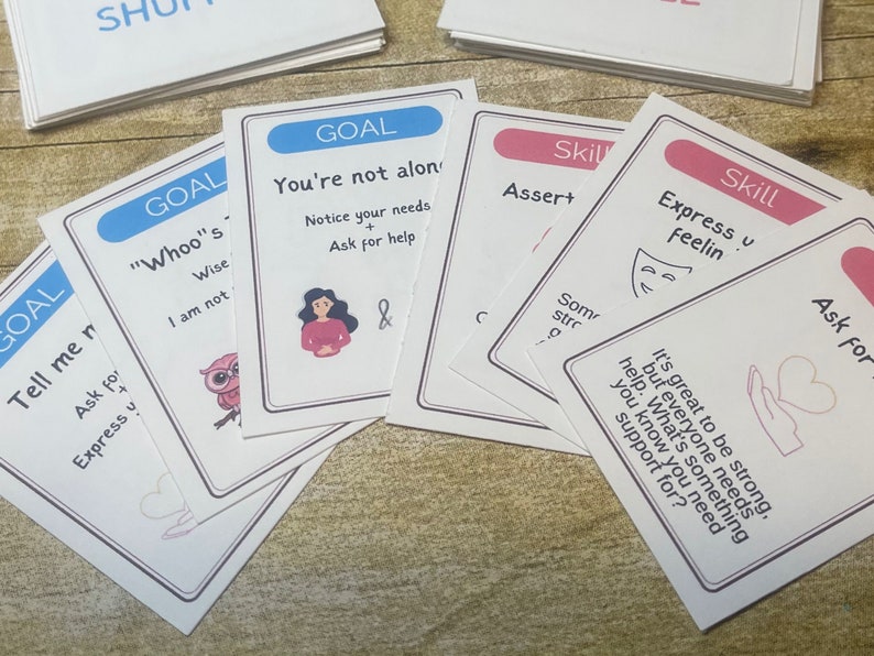May include: A set of colorful cards with the word "Goal" and "Skill" printed on them. The cards feature illustrations of a woman, an owl, a mask, and a hand with a heart. The text on the cards includes phrases like "You're not alone", "Notice your needs", "Ask for help", "Express your feelings", and "It's great to be strong".
