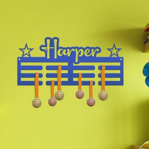May include: Blue medal display rack with the name "Harper" and stars on either side. The rack has orange medal hangers and is mounted on a yellow wall. There are several medals hanging on the rack.