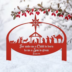 Könnte beinhalten: Ein rotes Krippen-Gartenschild aus Metall mit einem Stern, Figuren von Menschen und Tieren sowie dem Text "For unto us a Child is born to us a Son is given Isaiah 9:6", eingefasst in einen ovalen Rahmen mit zwei Erdspießen.